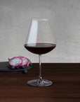 NUDE Salute Burgundy wine glass filled with red wine, beside dragon fruit and blueberries on a slate board