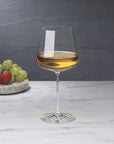 NUDE | Tom Dixon Splash White Wine glass filled with white wine on a marble surface, with grapes and strawberries on a stone board blurred in the background