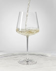 NUDE | Tom Dixon Splash White Wine glass with white wine actively pouring in and splashing against the bowl, set on a reflective marble surface.