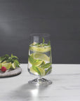 NUDE | Tom Dixon Splash Highball glass filled with water, lime wedges, and mint leaves on a marble surface, with more mint, lime, and berries on a stone board blurred in the background.