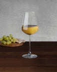 NUDE Salute white wine glass with white wine beside green grapes and bread on a wooden board