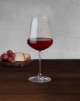 NUDE Salute red wine glass with red wine beside aged cheese and red grapes on a wooden board