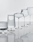 The five NUDE Splash glasses filled with water in an ascending row, including the Splash Red Wine glass, each showing the signature ripple foot base.