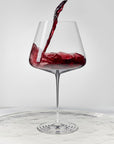 NUDE Splash Red Wine glass with red wine actively pouring in and splashing against the bowl, set on a reflective marble surface.