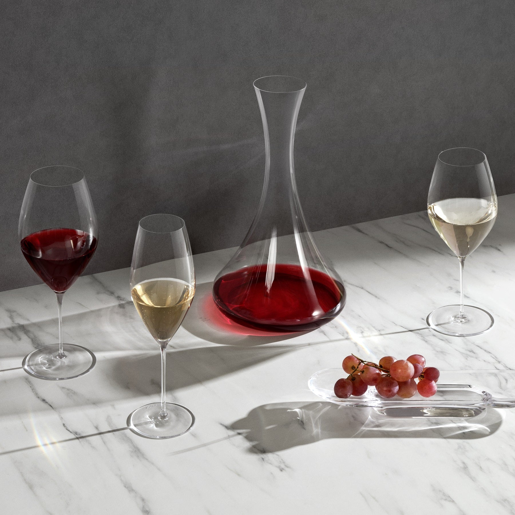 Cone shaped tall wine decanter in lead-free crystal, presented with red wine in it on a table with tablecloth surrounded by white, red and champagne glasses which are filled